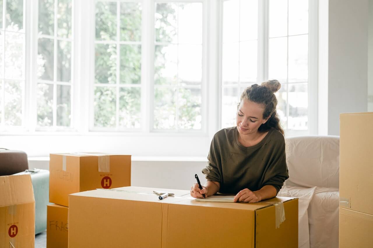 Woman writing a moving checklist on top of moving boxes