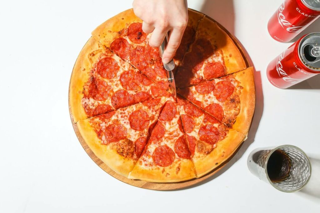 Someone cutting a pepperoni pizza with a pizza cutter